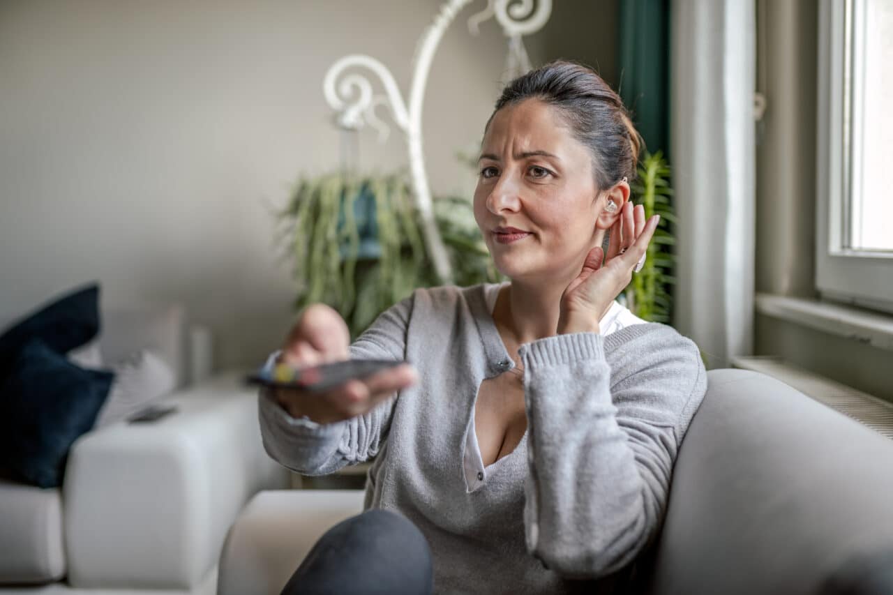 Woman adjusting her hearing aid while watching television.