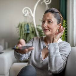 Woman adjusting her hearing aid while watching television.